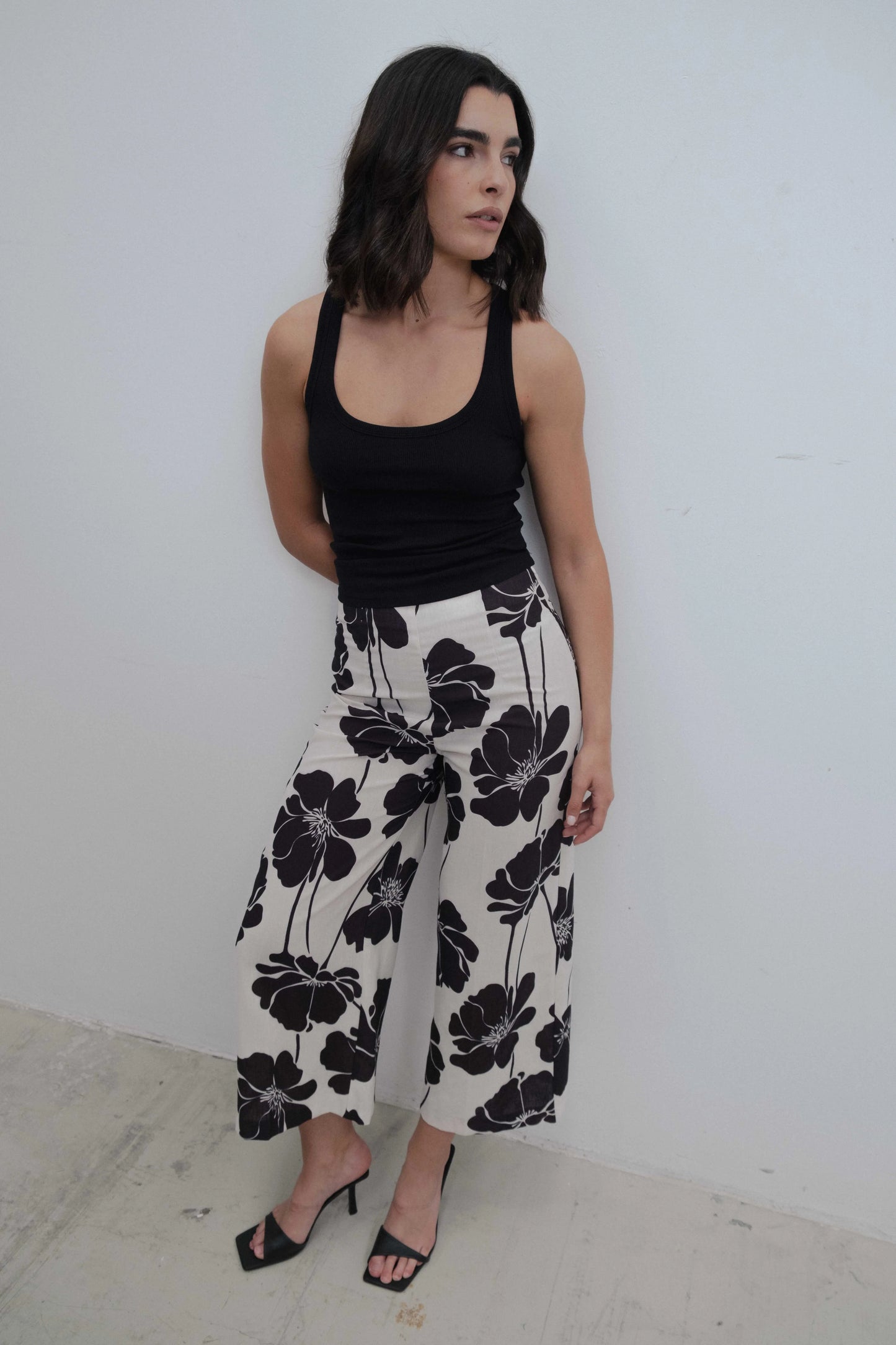 Modelo posando con pantalón culotte fluido de poliéster con estampado floral negro y blanco y top de tirantes negro.